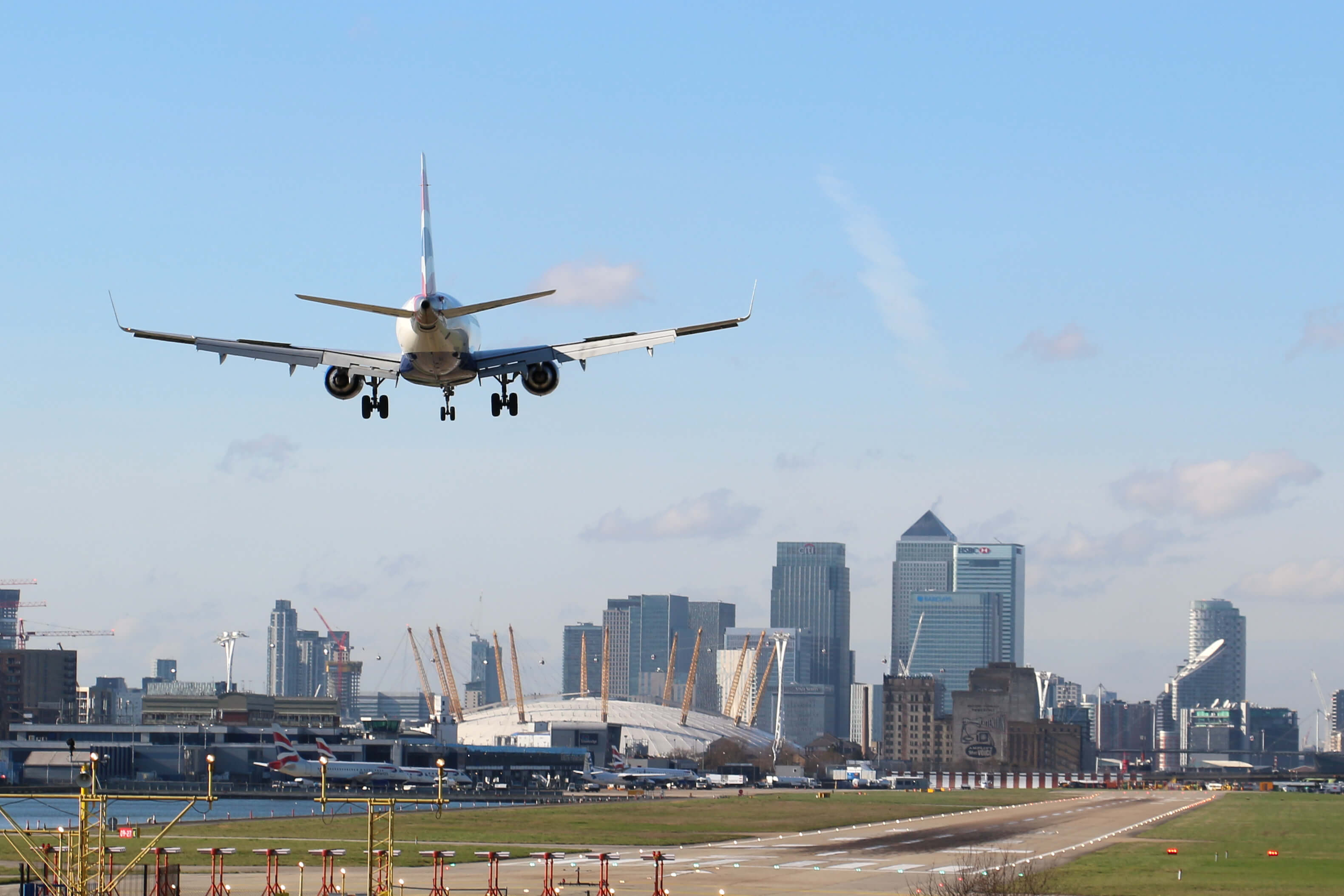 British Airways Plane landing at London's City Airport on a sunny day with Canary Wharf in the background